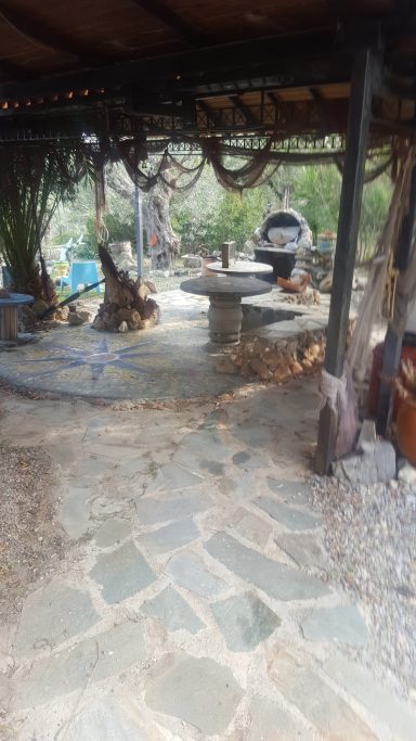 Gemütlicher Außenbereich mit Steintisch und Holzstühlen, umgeben von Pflanzen.