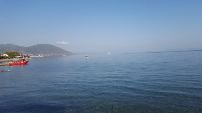 Ruhige See mit leicht bewölktem Himmel und Bergen im Hintergrund.